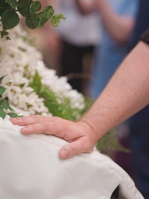 A man places his hand on the casket by the opening, spending a moment with his departed mother