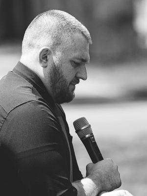 A man speaks about his mother in heartfelt stories, holding a microphone.