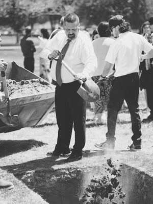 A man casts a shovel full of dirt on top of the lowered casket