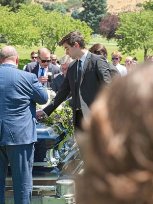 An elder son lays his boutonniere on the casket of his father