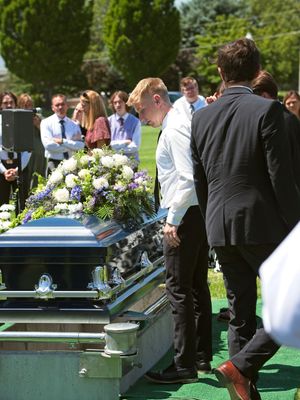 The younger son stands at the casket of his father after they place his casket over the grave.