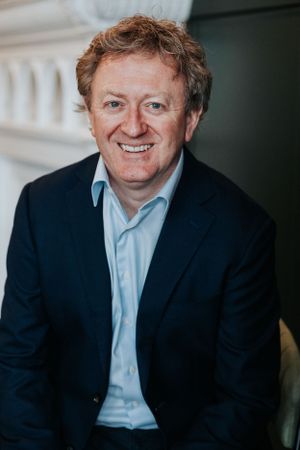 Professional portrait of a person wearing a navy blazer and light blue shirt smiling at the camera.