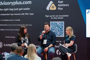 Three professionals engage in a panel discussion at App Advisory Plus booth during a business conference event.