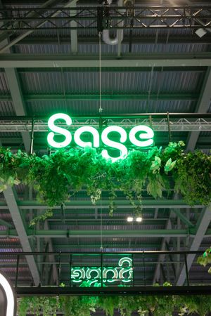 Sage neon green logo sign hanging from ceiling with lush green foliage decoration at a trade show booth.