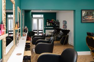 Stylish hair salon interior with teal walls, black leather chairs, gold-framed mirrors, and herringbone wood floors.