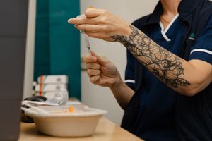 Tattooed nurse preparing a syringe injection in a medical clinic setting.