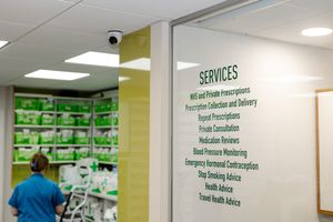 Pharmacy interior showing services list on glass door including NHS prescriptions, medication reviews, and health advice.