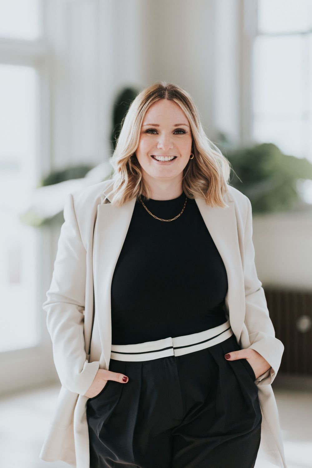 Professional business portrait featuring stylish cream blazer over black outfit with waist belt in bright indoor setting.
