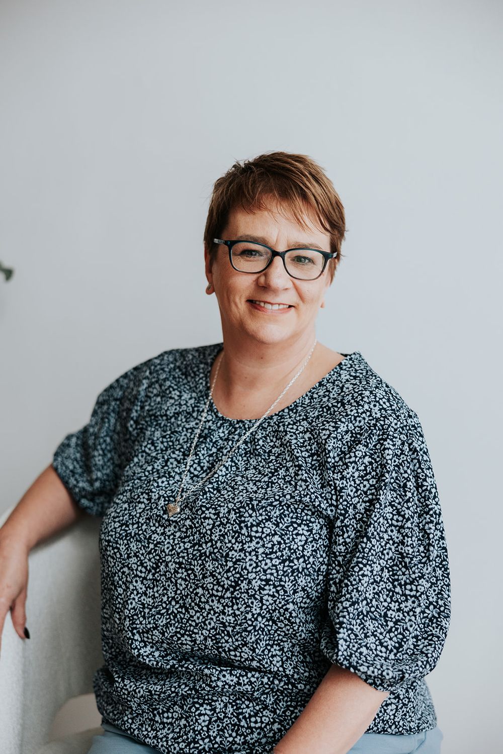 Professional portrait of a person wearing glasses and a patterned shirt against a light gray background.