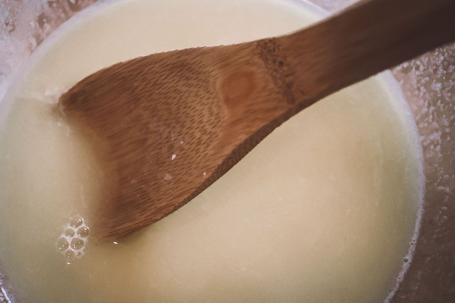 A wooden spoon stirs creamy white sauce or liquid in a bowl during cooking preparation.