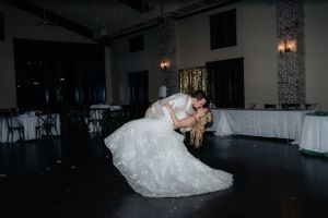 A romantic dip on the dance floor during a wedding reception in a darkly lit ballroom.