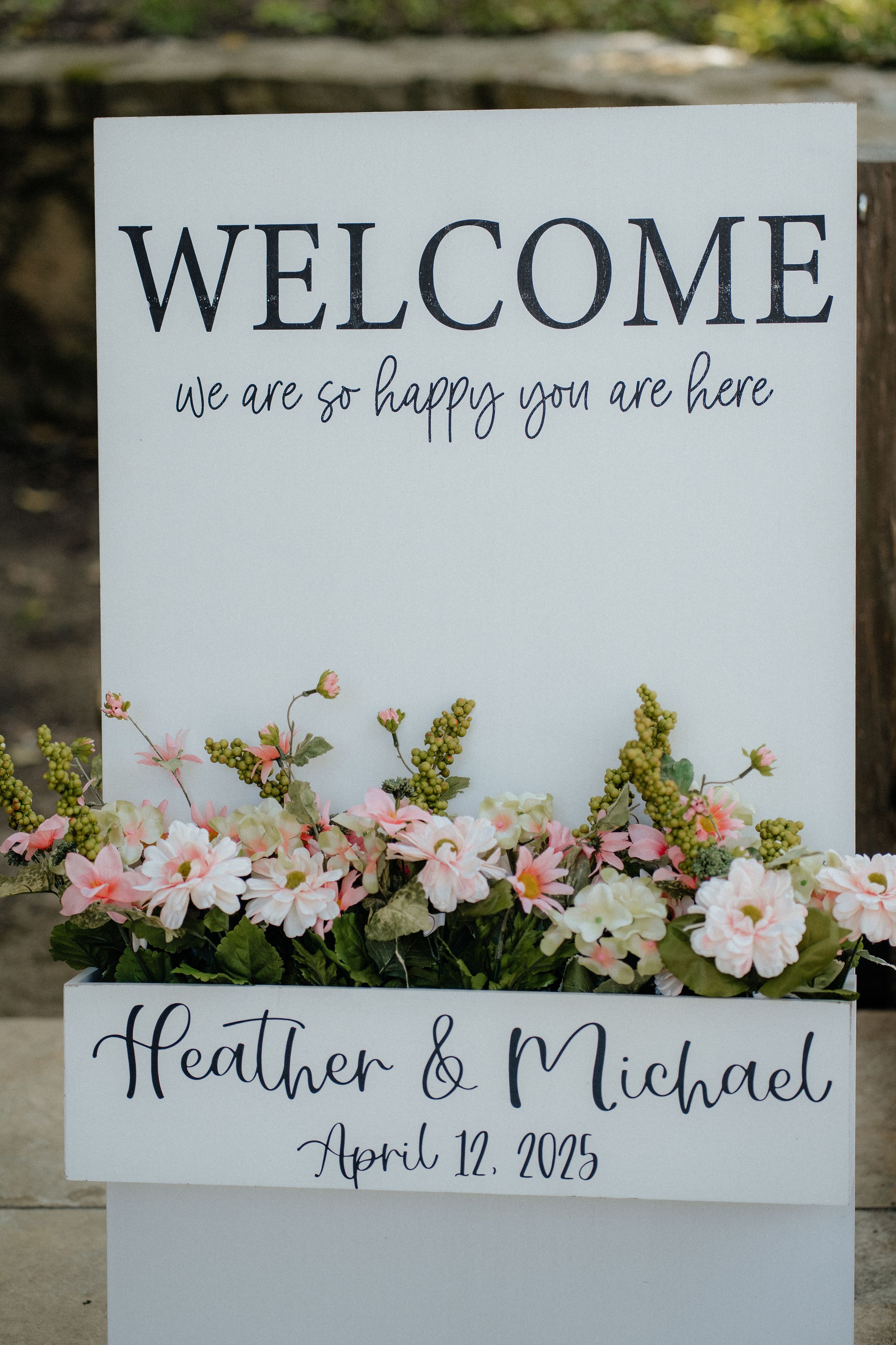 Welcome sign with floral decorations announcing a spring wedding celebration.