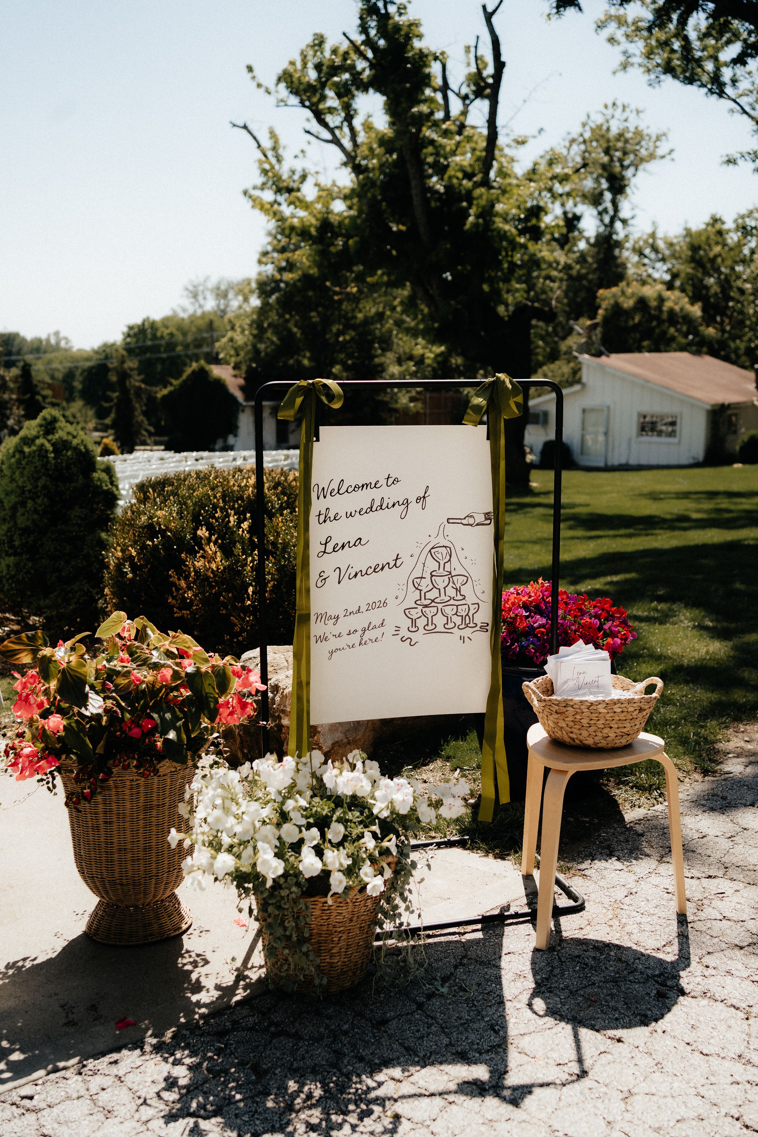 Outdoor wedding welcome sign for Lana and Vincent surrounded by colorful floral arrangements on a sunny day.