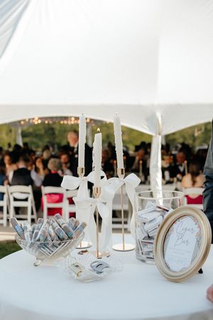 Elegant outdoor wedding reception table with white candles, gold candelabra, and framed signage under a white tent.