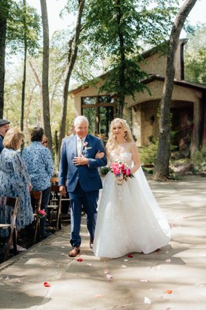 Wedding ceremony processional on stone pathway with rose petals scattered on the ground.