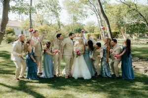 Wedding party in tan and blue attire posing together on sunny lawn.