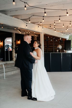 Bride and groom share first dance under warm string lights in elegant indoor wedding venue.