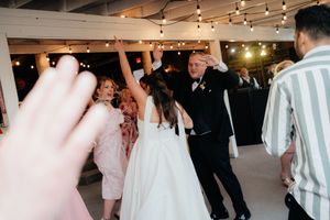 Bride and groom dancing joyfully with guests at a wedding reception under warm string lights.