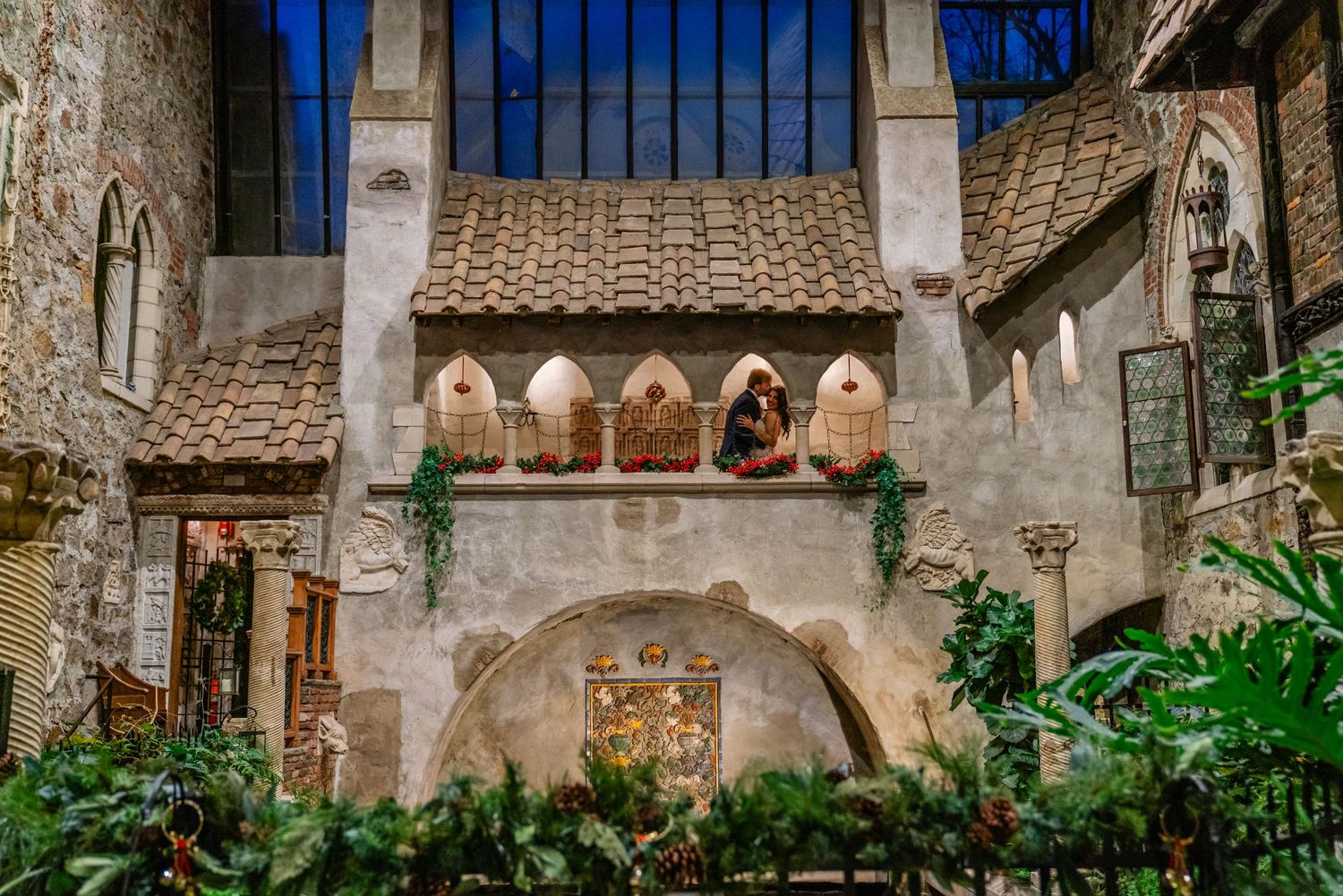 A rustic stone balcony with arched windows overlooking an indoor garden.