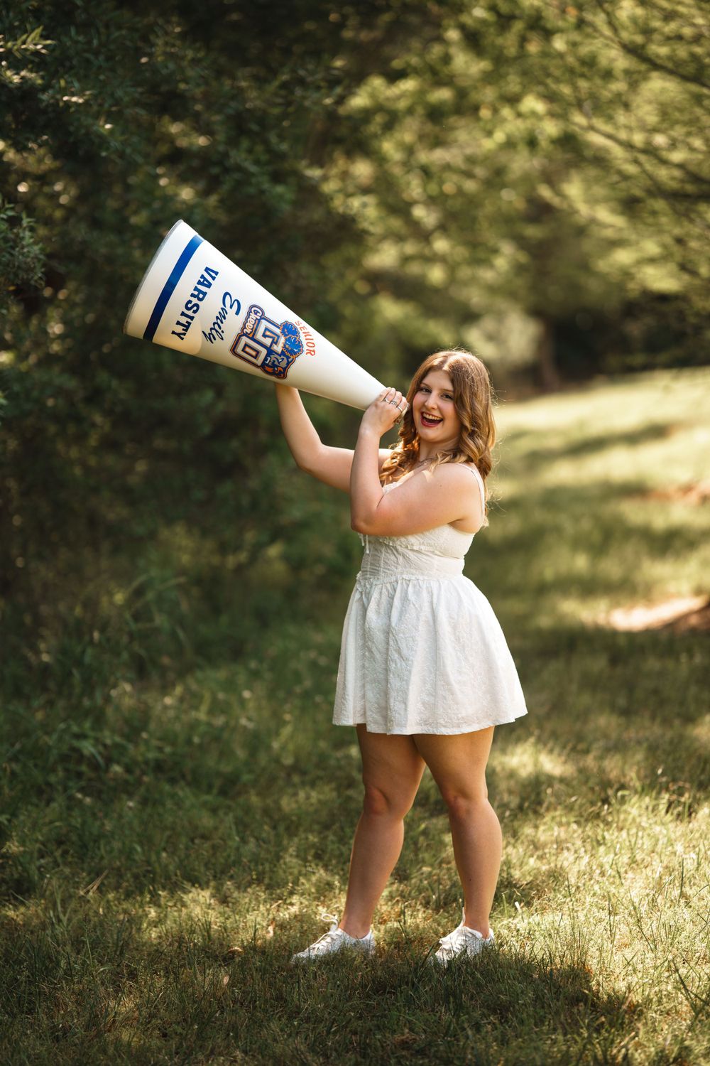 Person in white dress holding large Kentucky megaphone prop in sunny outdoor setting.