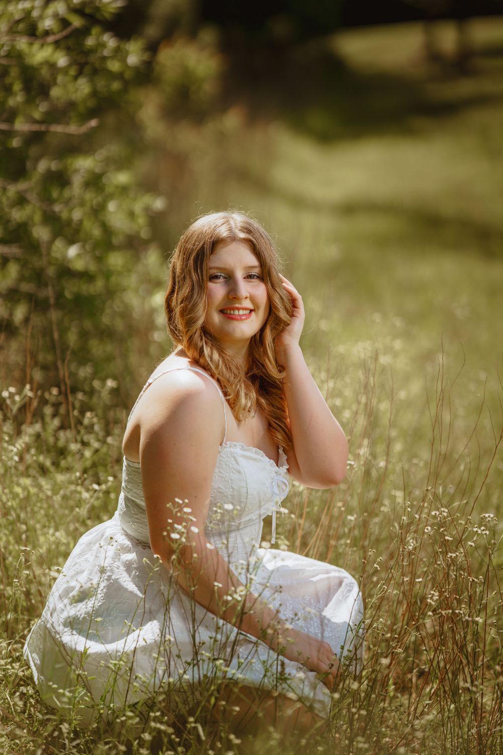 A person in a delicate white lace dress sits in a golden sunlit meadow of wildflowers on a warm summer day.
