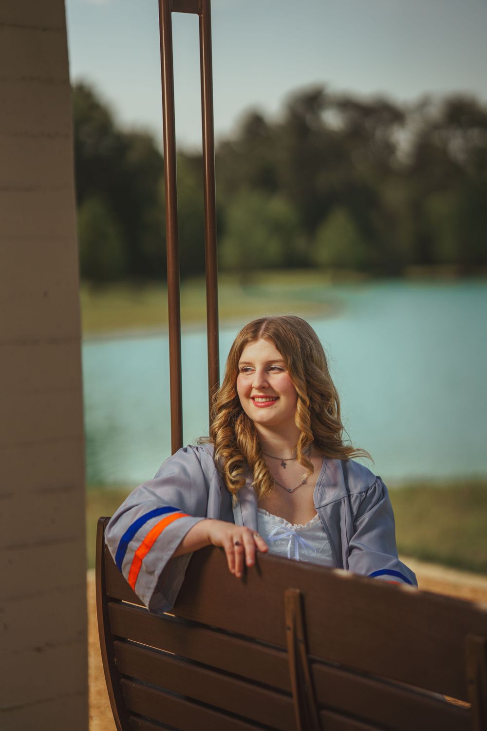 Portrait of someone sitting on a wooden bench near a lake on a sunny day, wearing a blue shirt.