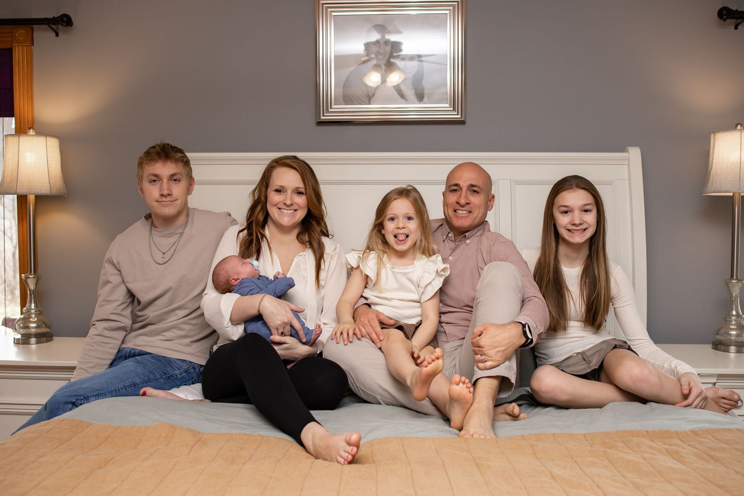 Central Illinois photographer captures a family sitting on a bed smiling during a newborn session in Springfield, IL