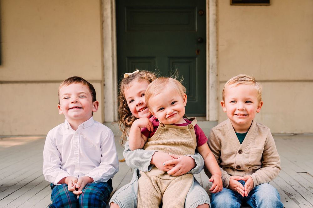 Five children sitting together on a wooden porch laughing and playing while dressed in casual clothing.