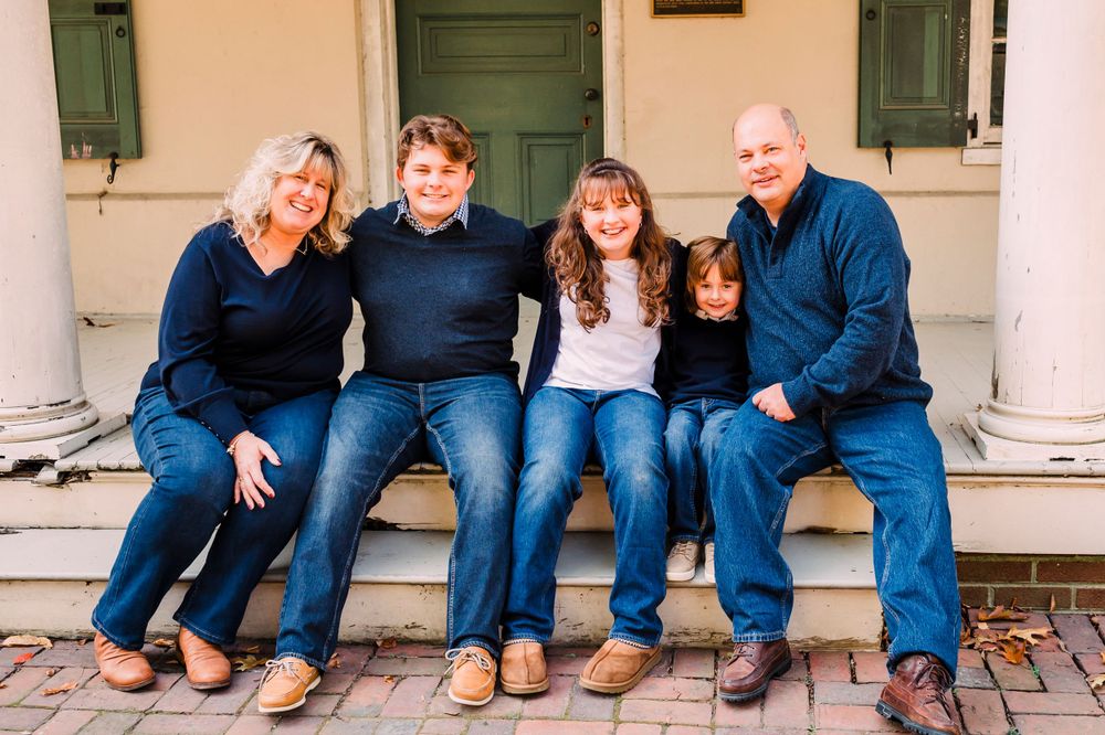 A family of five sits together on a porch step wearing coordinated casual clothing in shades of blue.