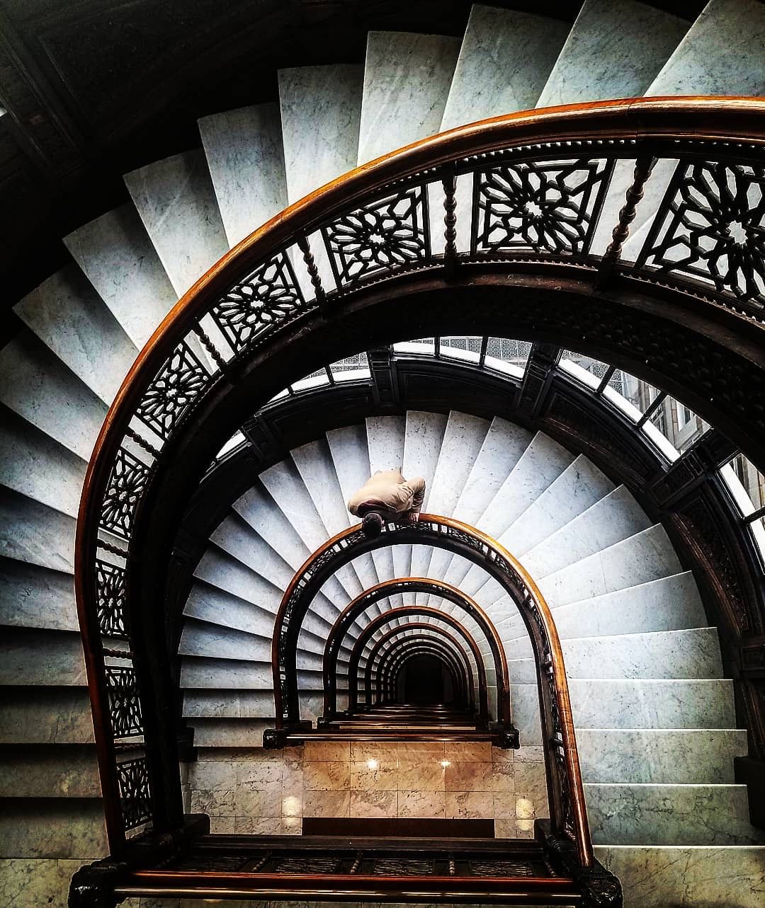 Spiral staircase with ornate metal railings and dramatic lighting creating a tunnel effect.