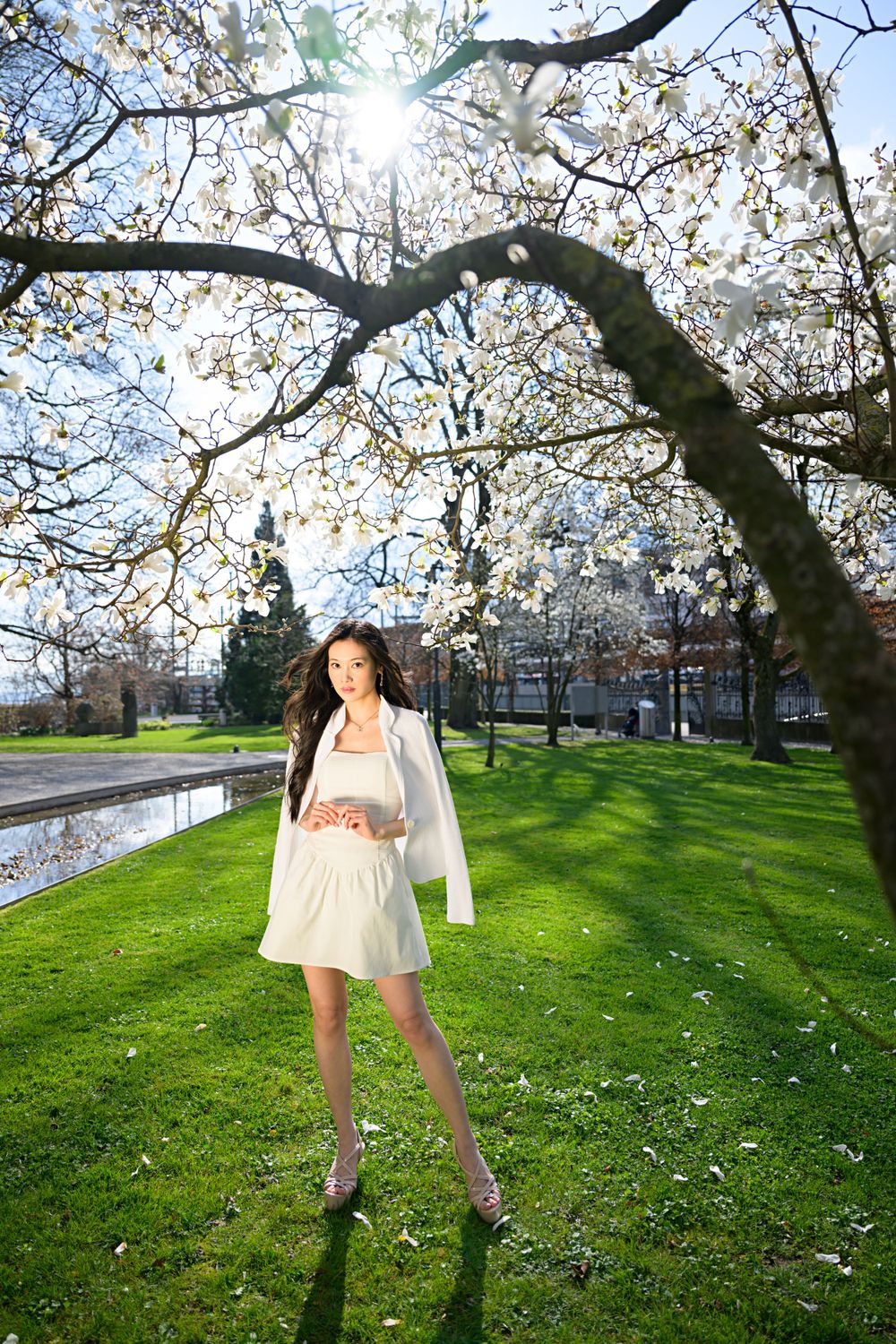 Model posing under spring blossoms in Switzerland. White outfit, minimal styling, clean beauty for fashion portfolio.High Quality photos