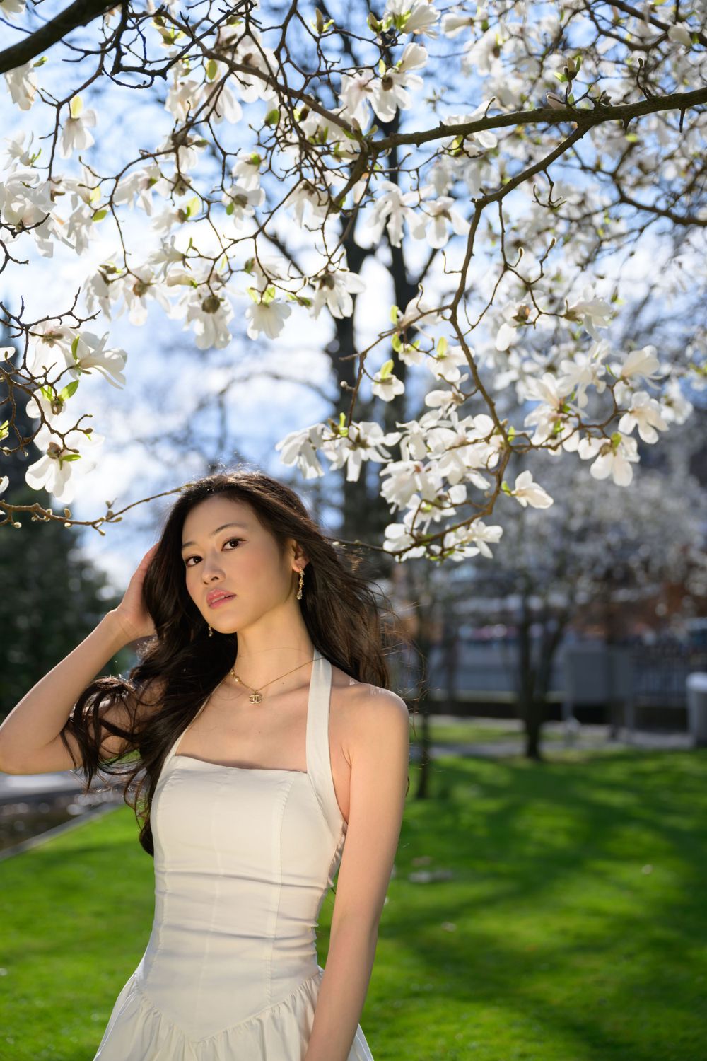 Spring fashion photoshoot in Zurich with model in white dress under magnolia blossoms. Outdoor shoot with natural light and soft styling.und