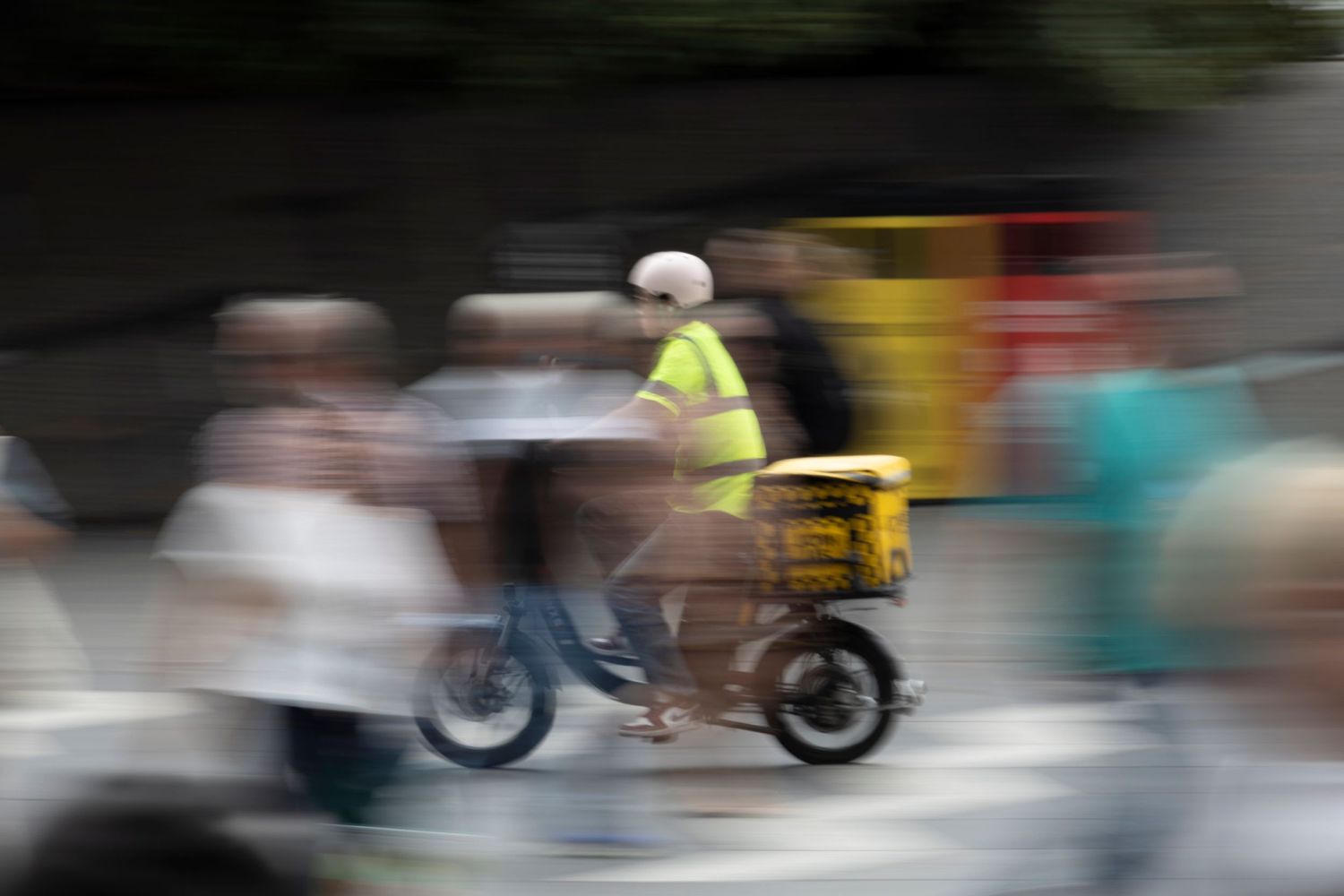 Motion-blurred image of a delivery scooter speeding through a busy street filled with pedestrians.