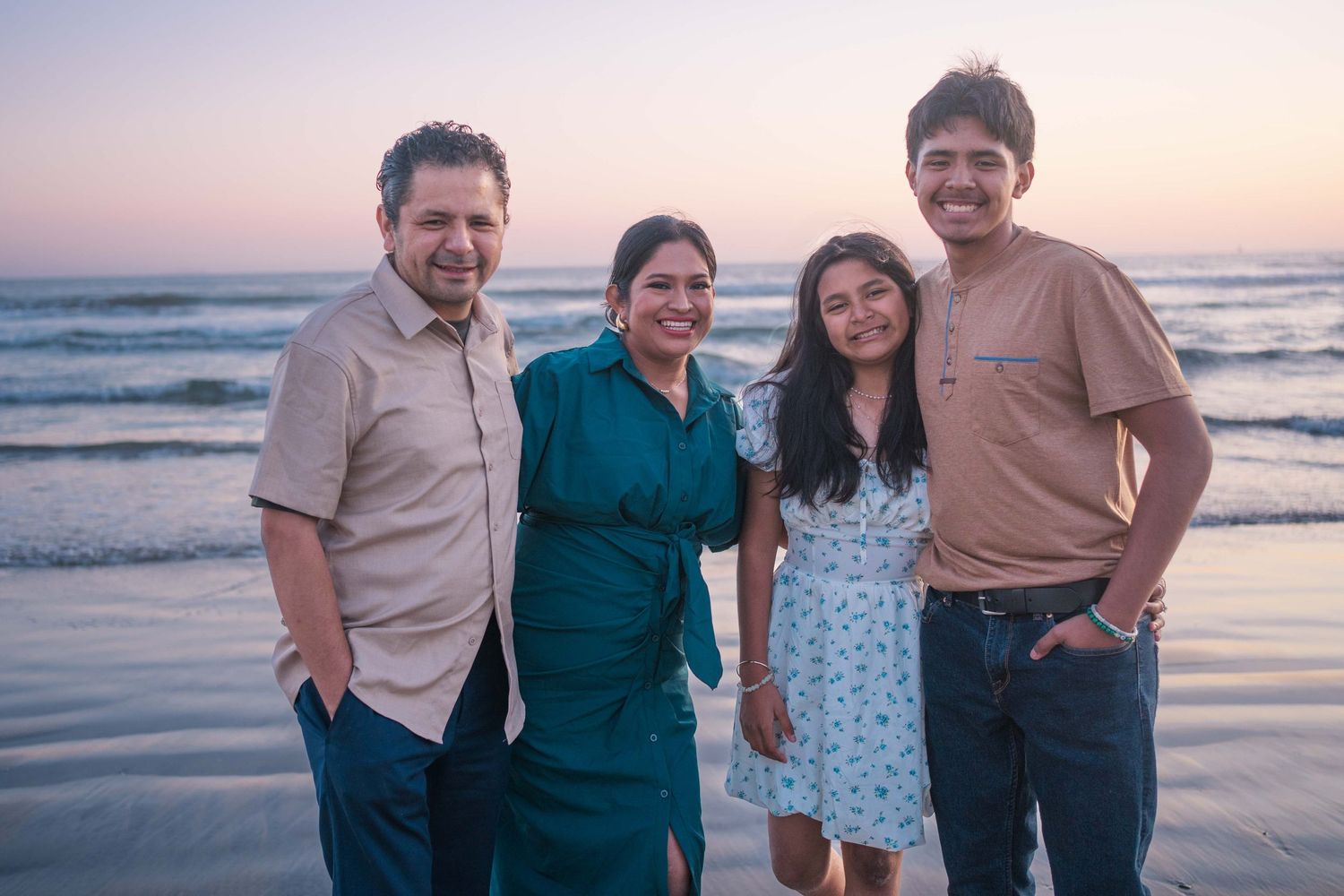Family members walk along the shoreline during golden hour at the beach.