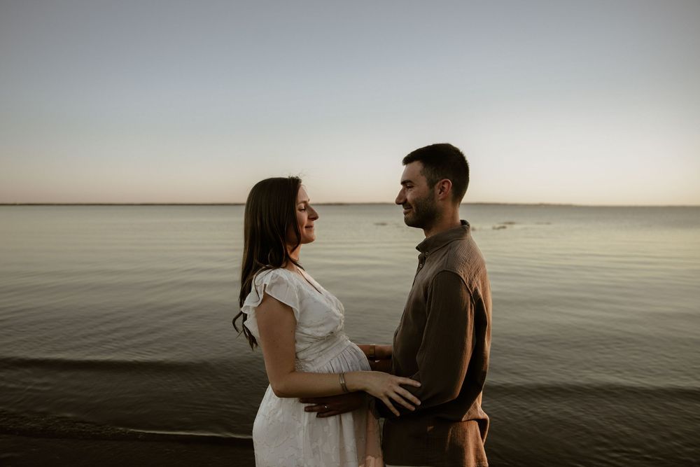 A couple shares an intimate moment at sunset by a serene waterfront setting.