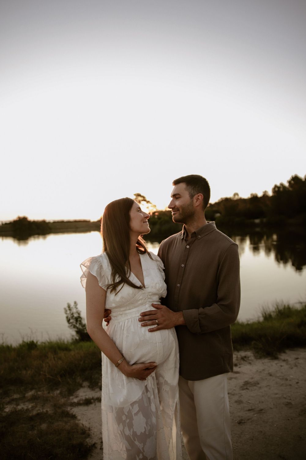 Couple in wedding attire sharing an intimate moment against a serene lakeside backdrop during sunset.