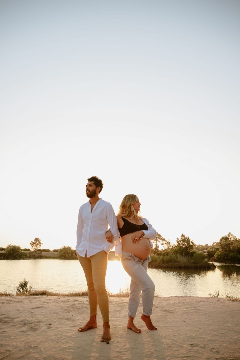 A couple walking on a sandy beach during golden hour sunset by the water's edge.