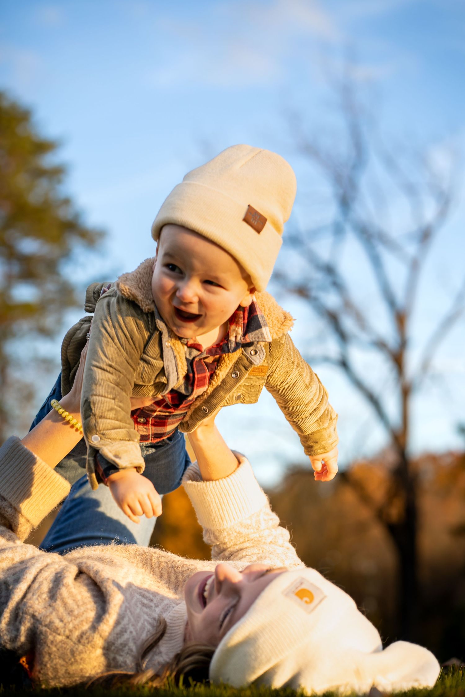 a toddler smiling a gasping with joy while he's lifted up in the air in a sunny autumn day