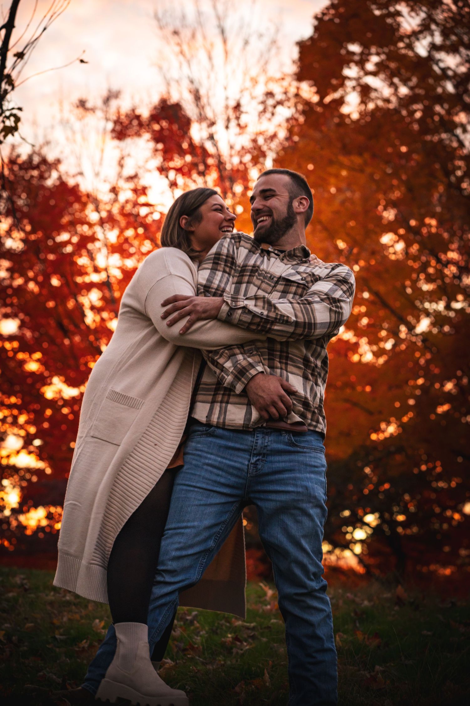 a woman running out and embracing her partner, who is grabbing her arms. both are laughing as the orange leaves fall behind them. the sun