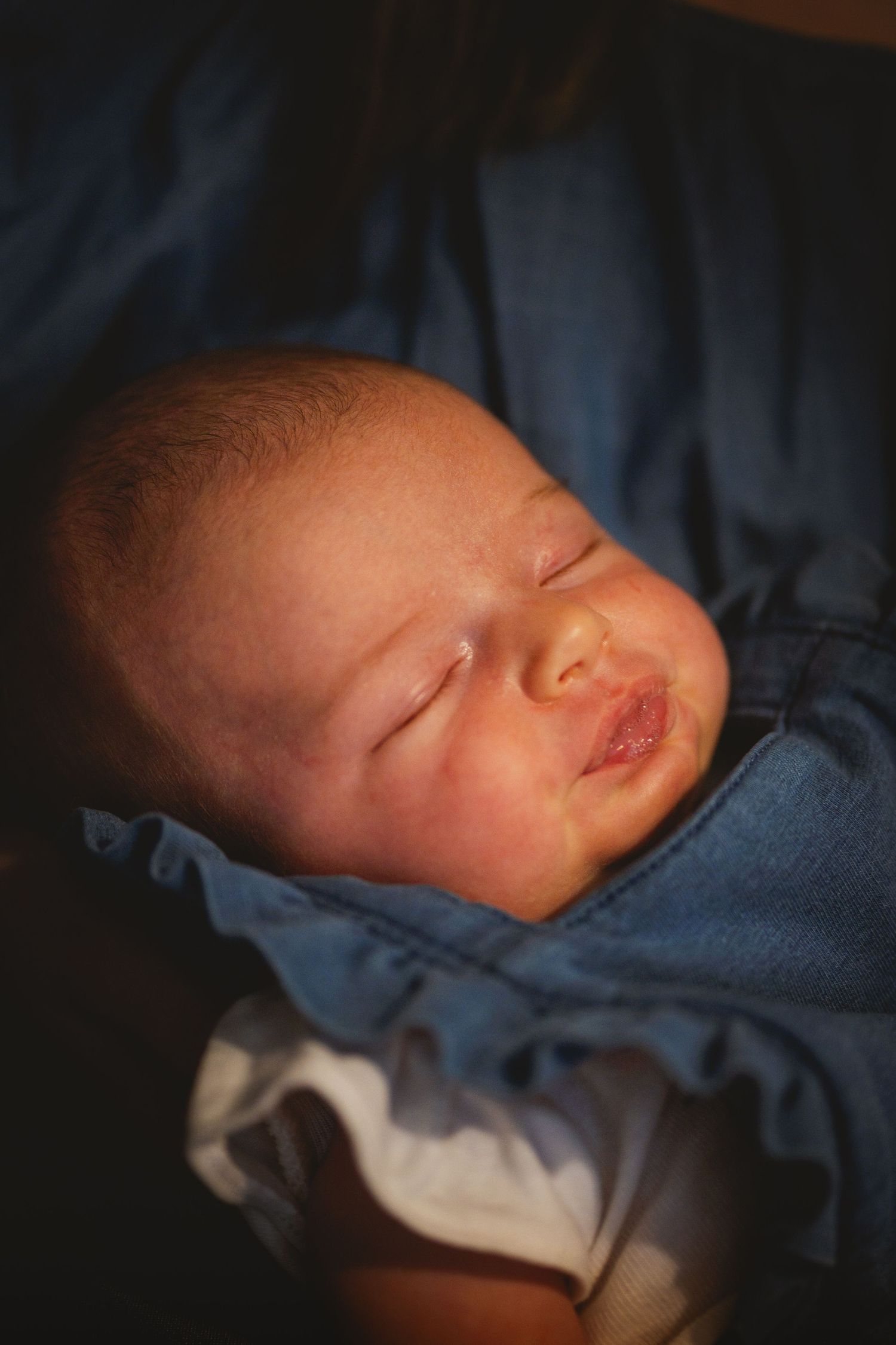 Peaceful newborn baby sleeping soundly wrapped in soft blue blanket in dim lighting.