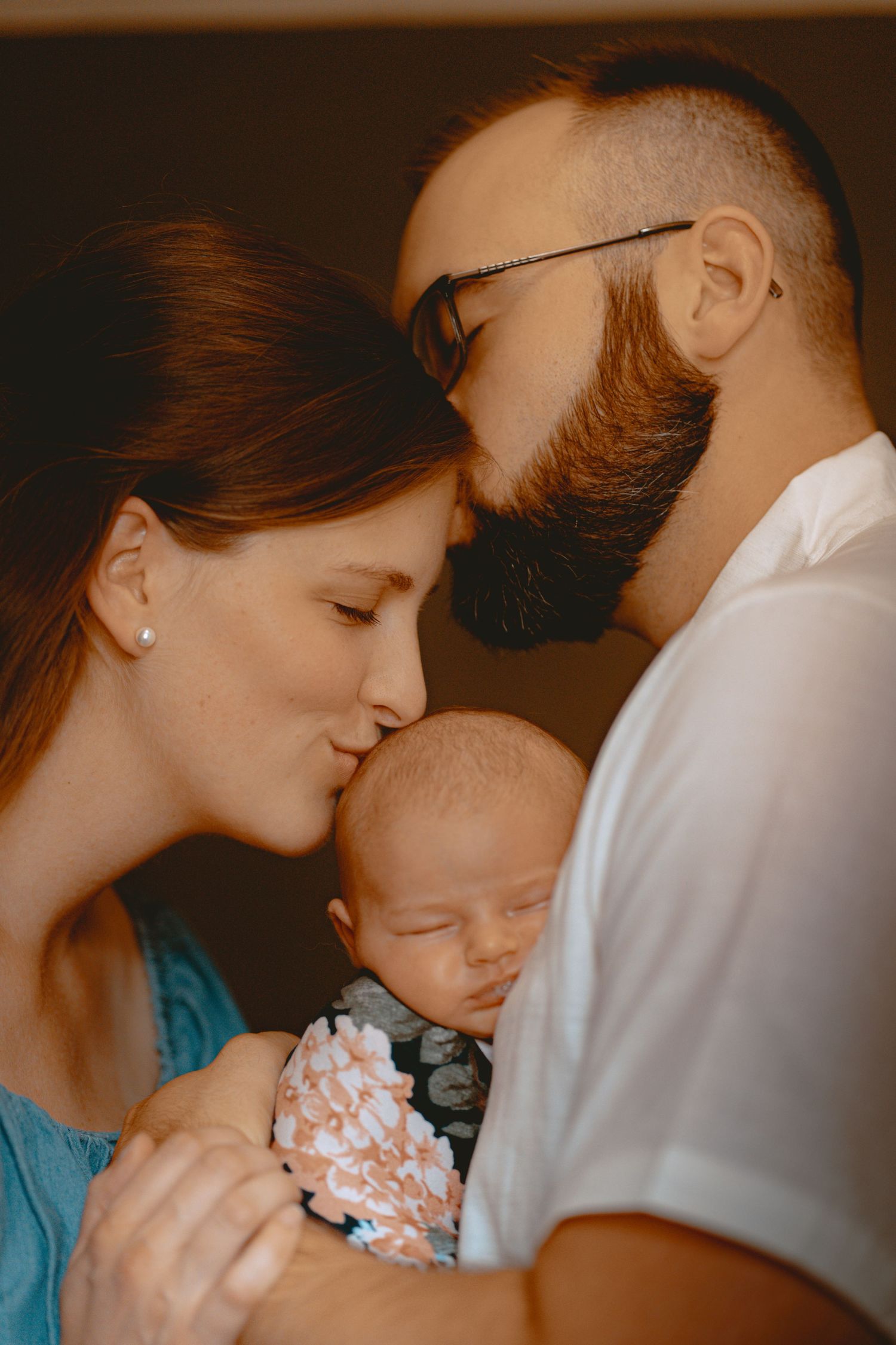 A tender family moment showing three connected figures sharing gentle kisses against a warm brown background.