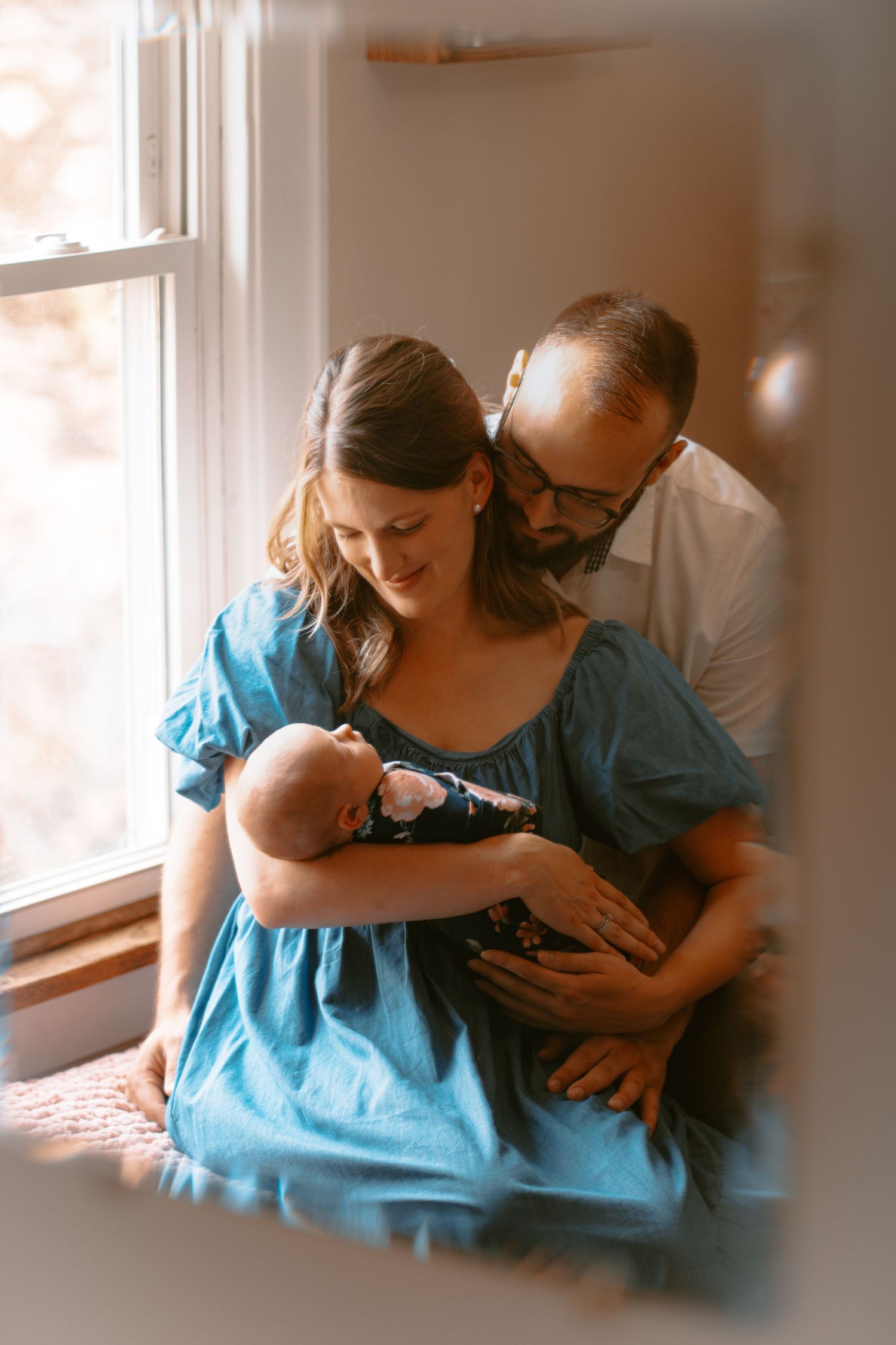 A series of intimate hospital photos showing a couple bonding with their newborn baby near a sunlit window.