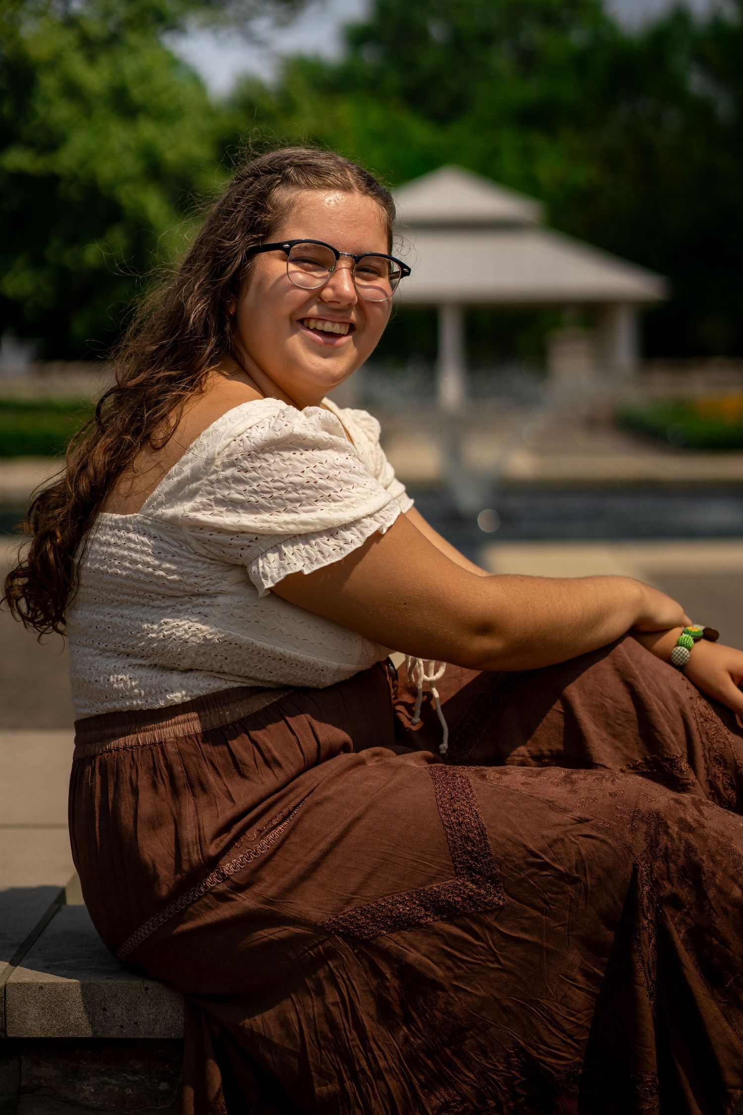 Person in vintage brown dress and lace top lounging on stone wall outdoors.
