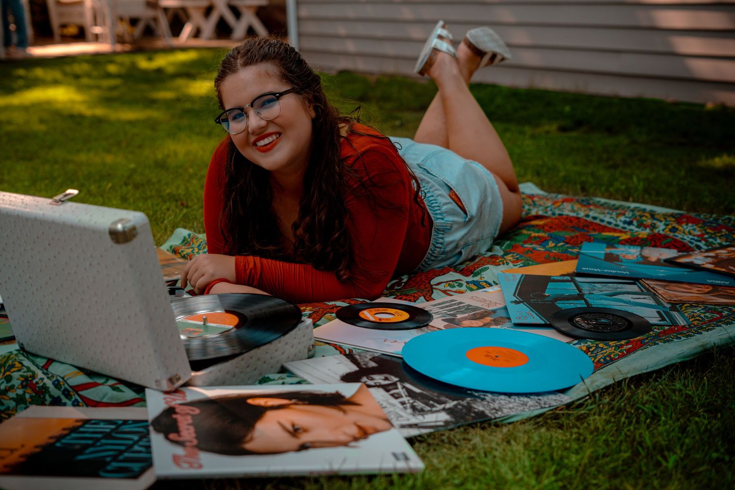 Student studying outdoors on green grass with laptop and colorful vinyl records spread around them.