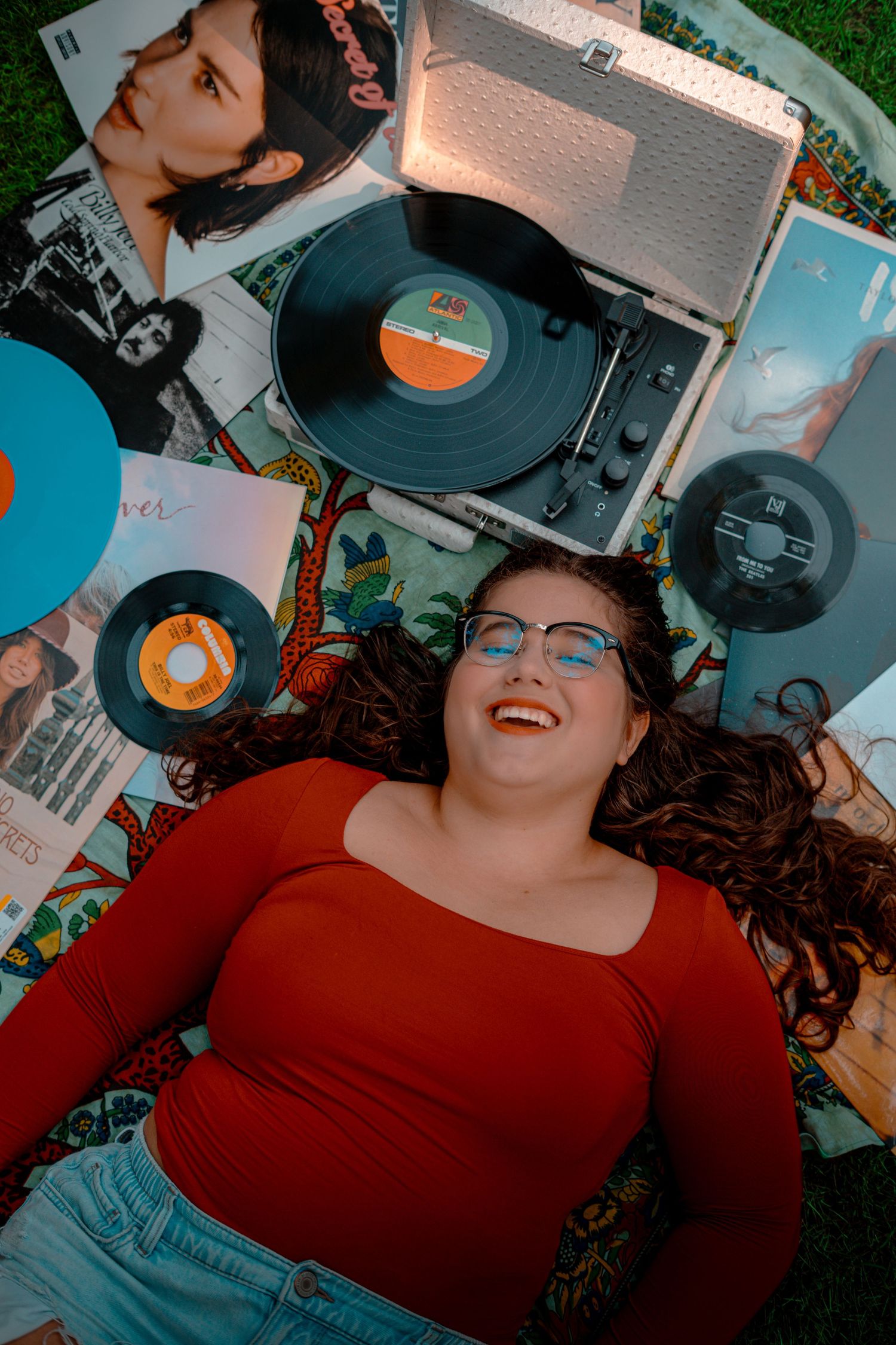 Person in red top laying among vinyl records during retro-styled photoshoot.