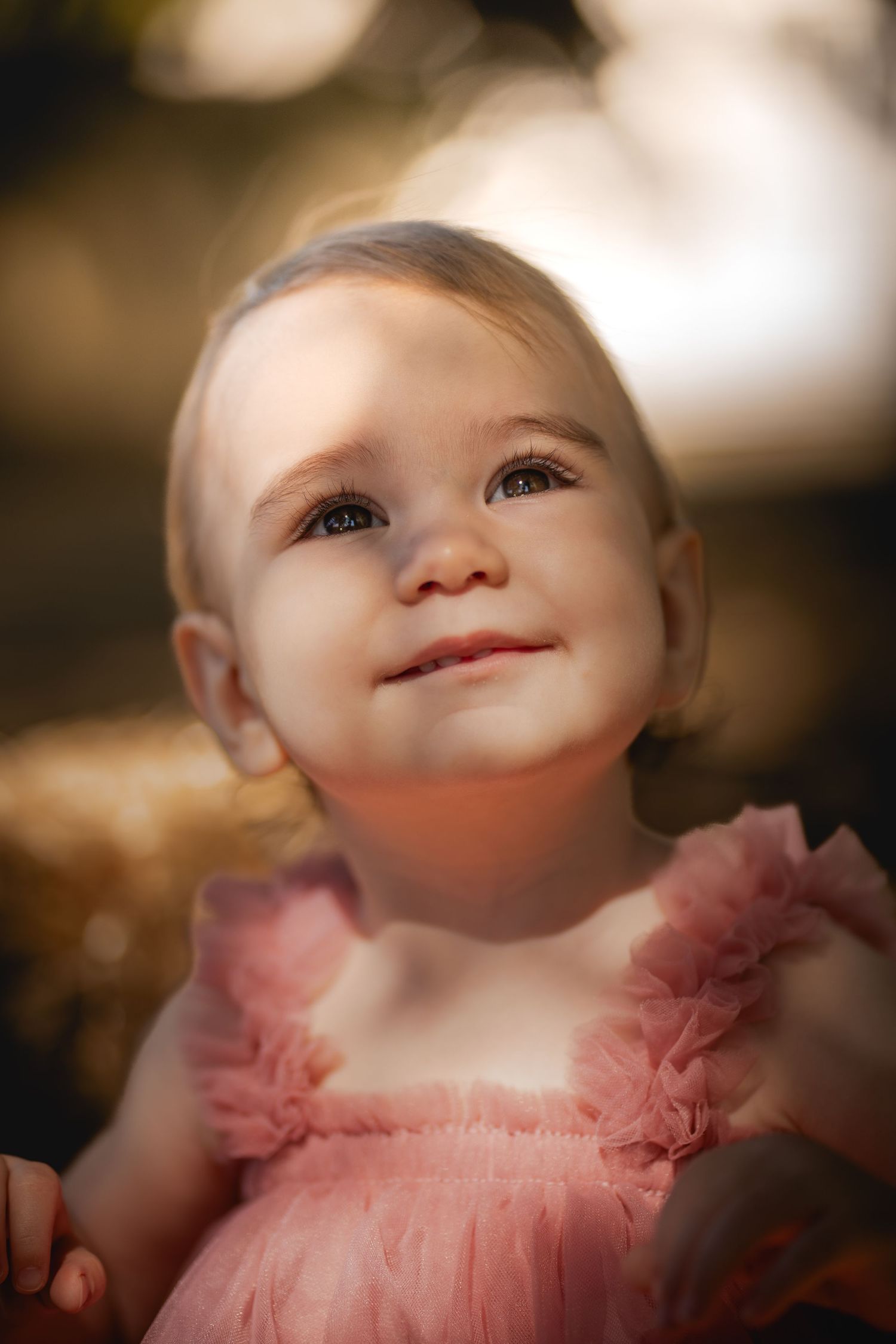 Series of closeup baby portrait shots in pink dress with soft bokeh background showing expressions of joy and wonder.