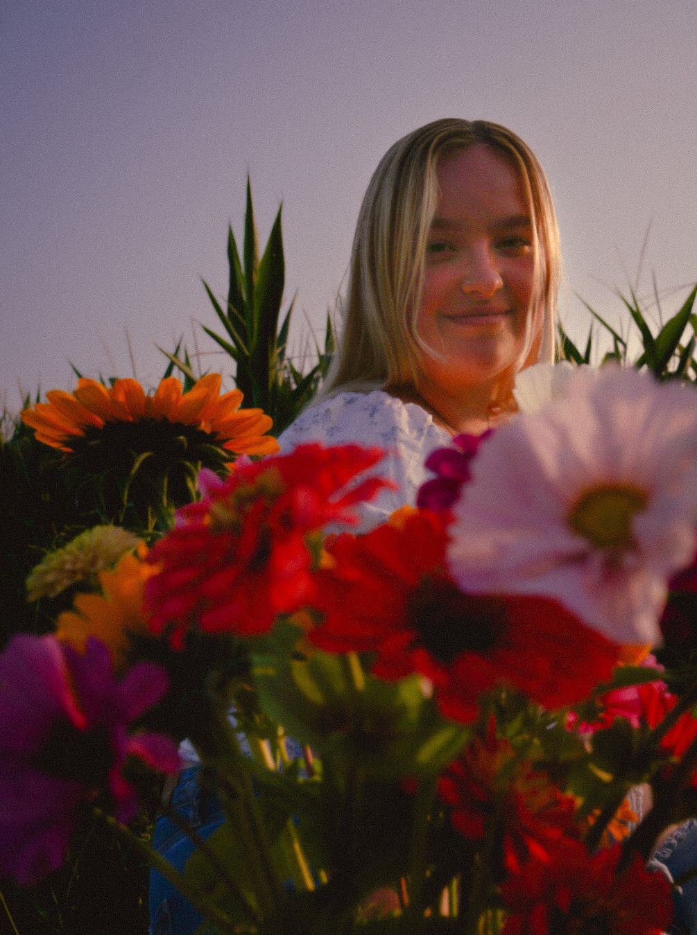 a girl standing in a cornfield. holding a bouquet of flowers and smiling while the sun highlights her smile