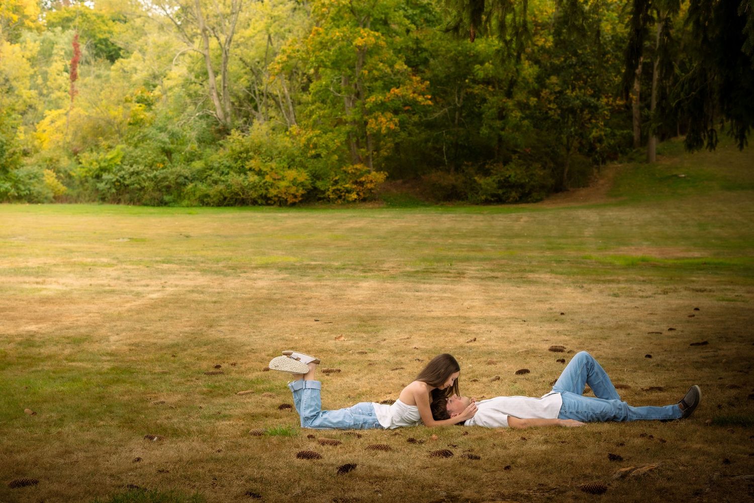People relaxing on blankets in a grassy field surrounded by autumn trees on a sunny afternoon.
