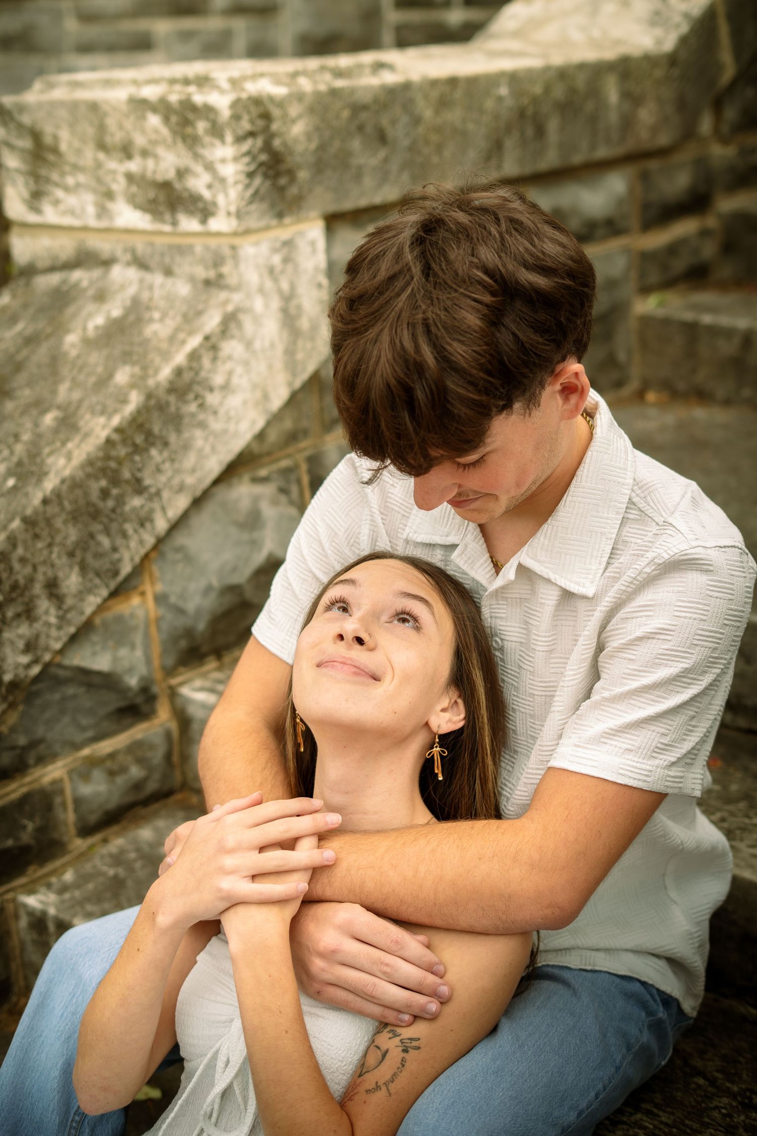 A romantic couple embraces tenderly while sitting together outdoors on stone steps.