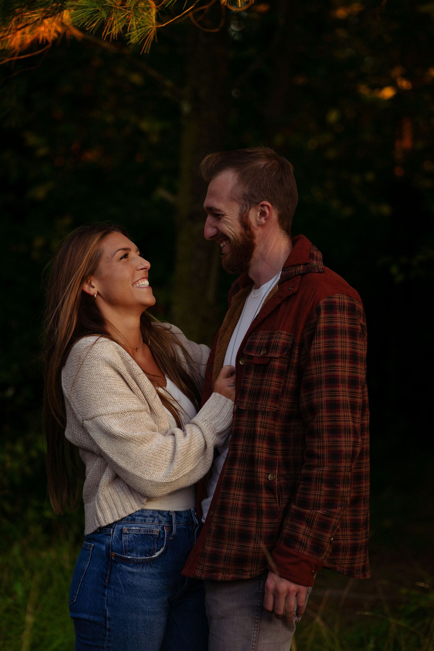 a happy couple laughing and smiling at each other while taking engagement photos. her hand on his chest while they look at each other